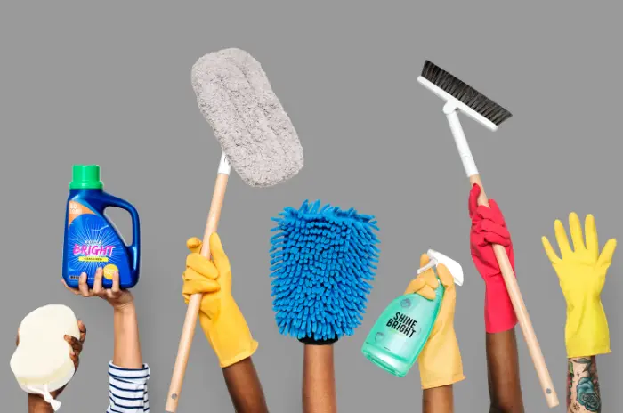 Various hands holding cleaning supplies including gloves, brushes, a mop, detergent, and spray bottle against a grey background