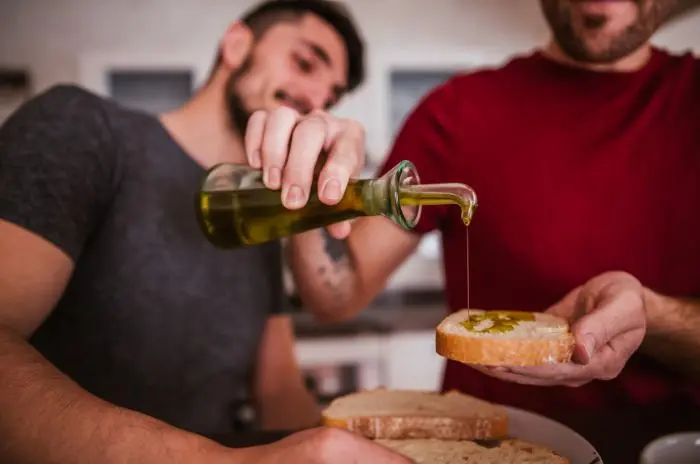 Man pouring olive oil onto a slice of bread in a kitchen